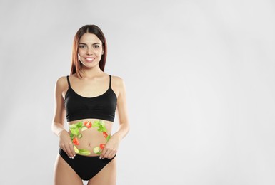 Slim young woman wearing underwear and images of vegetables on her belly against light background. Healthy eating