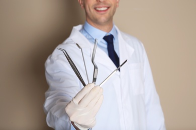 Male dentist holding professional tools on color background, closeup
