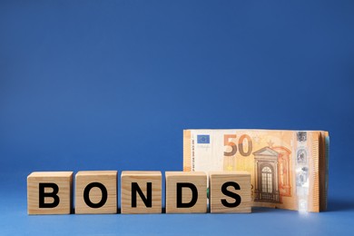Photo of Word Bonds made of wooden cubes with letters and euro banknotes on blue background