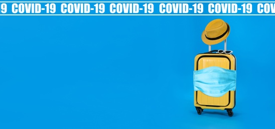 COVID-19 pandemic, travel during coronavirus outbreak. Suitcase with protective mask on blue background, space for text 