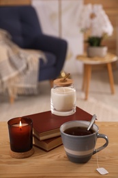 Cup of tea, books and candles on wooden table in living room. Interior design