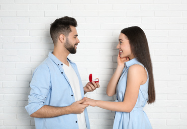 Man with engagement ring making marriage proposal to girlfriend near white brick wall