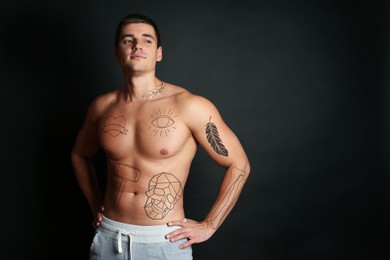 Handsome man with beautiful tattoo sketches on black background. Space for text