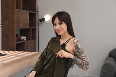 Photo of Beautiful woman with tattoos on arm at table indoors