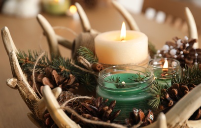 Burning scented conifer candles with Christmas decor on table, closeup