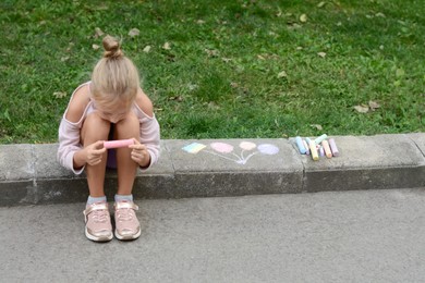 Photo of Little child chalk piece sitting on curb outdoors, space for text