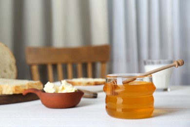 Photo of Jar with honey, butter, bread and milk served for breakfast on white wooden table
