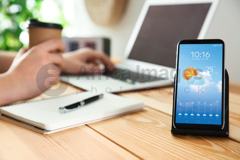 Image of Man working at table and smartphone with open weather forecast app indoors
