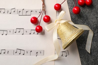 Photo of Golden shiny bell with white bow, decorative berries and music sheets on grey textured table, flat lay and space for text. Christmas decoration