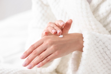 Young woman applying hand cream indoors, closeup. Beauty and body care