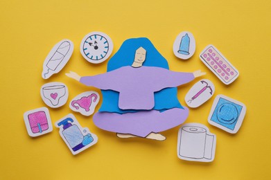 Photo of Woman paper figure with personal hygiene products on yellow background, flat lay