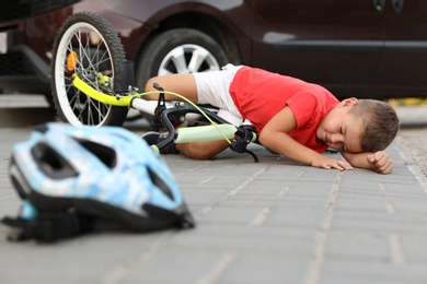 Little boy fallen from bicycle after car accident and helmet on road
