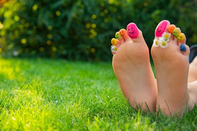 Photo of Teenage girl with chamomiles and smiling faces drawn on toes outdoors, closeup. Space for text