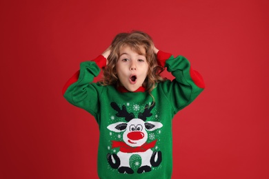 Surprised little girl in green Christmas sweater against red background