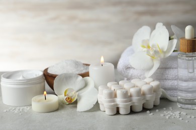 Beautiful composition with different spa products, burning candles and flowers on light grey table