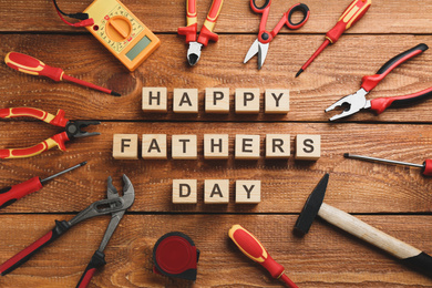 Wooden cubes with phrase HAPPY FATHER'S DAY and different tools on wooden background, flat lay