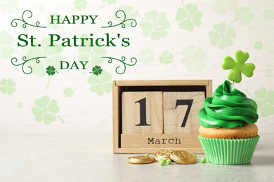 Delicious decorated cupcake, wooden block calendar and coins on light table. St. Patrick's Day celebration