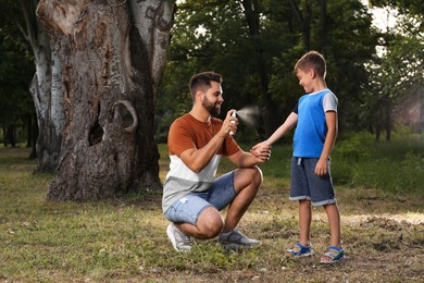 Man applying insect repellent on his son's leg in park. Tick bites prevention