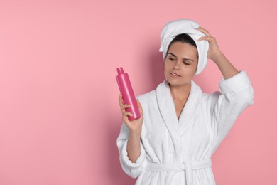 Beautiful young woman holding bottle of shampoo on pink background, space for text