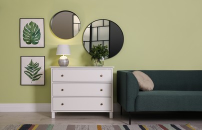 Photo of White chest of drawers with lamp, sofa and mirrors on wall in living room. Interior design