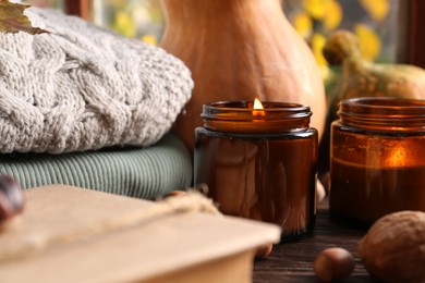 Burning scented candles, warm sweaters, book and pumpkins on wooden table, closeup. Autumn coziness