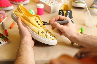 Man painting on sneaker at table, closeup. Customized shoes