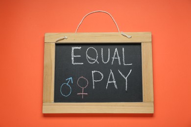 Photo of Blackboard with words Equal Pay and gender symbols on orange background, top view