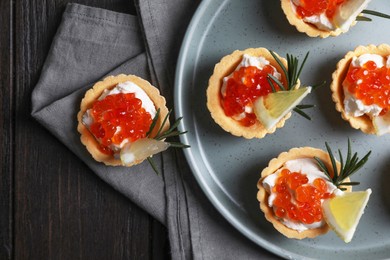 Photo of Delicious tartlets with red caviar and cream cheese served on wooden table, top view