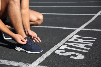 Sporty man tying shoelaces in front of starting line at stadium, closeup
