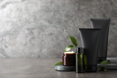 Facial cream and other men's cosmetic with green leaves on grey stone table. Mockup for design