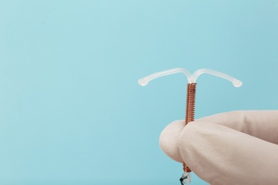 Doctor holding T-shaped intrauterine birth control device on light blue background, closeup. Space for text