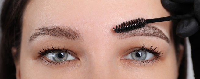 Photo of Beautician brushing woman's eyebrows before tinting, closeup