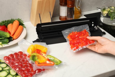 Woman using sealer for vacuum packing with plastic bag of red pepper at white table, closeup