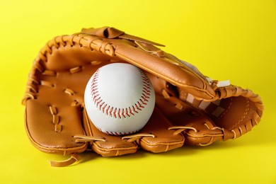 Photo of Catcher's mitt and baseball ball on yellow background. Sports game