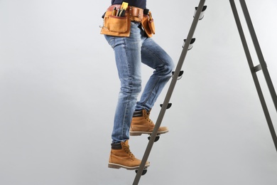 Professional builder climbing up metal ladder on grey background, closeup of legs