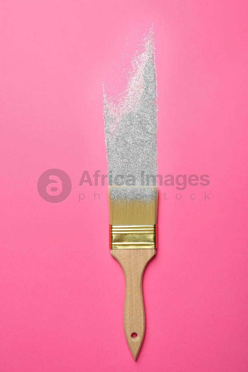 Brush painting with silver glitter on pink background, top view. Creative concept