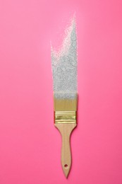 Photo of Brush painting with silver glitter on pink background, top view. Creative concept