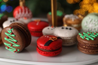 Beautifully decorated Christmas macarons on stand against blurred festive lights, closeup
