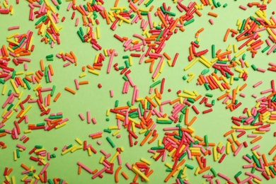 Colorful sprinkles on green background, flat lay. Confectionery decor