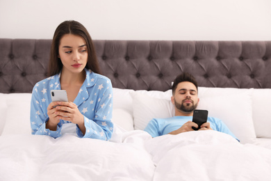 Young couple with smartphones in bed at home
