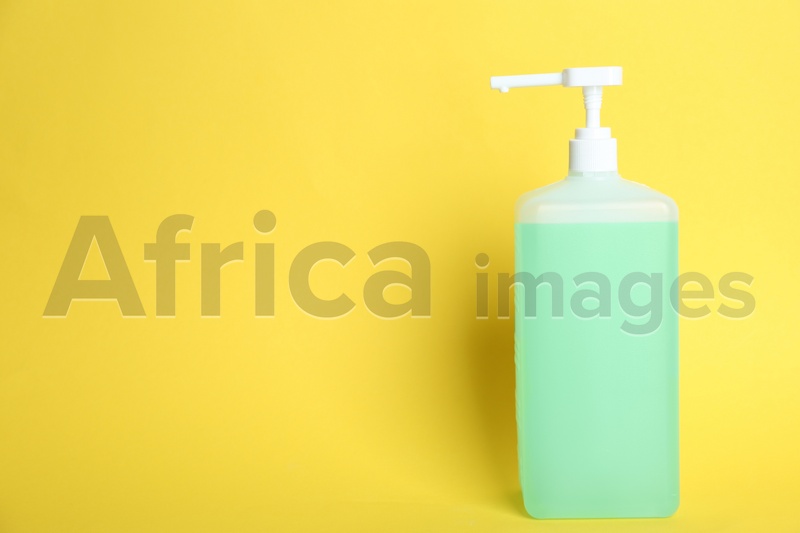 Dispenser bottle with green antiseptic gel on yellow background. Space for text