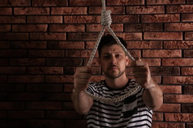 Depressed man with rope noose near brick wall