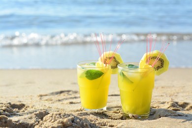 Glasses of refreshing drink with kiwi and mint on sand near sea. Space for text