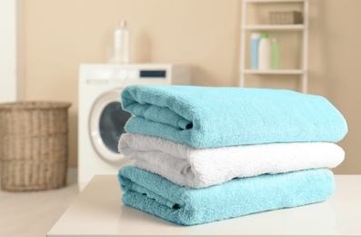 Stack of clean soft towels on table in laundry room. Space for text
