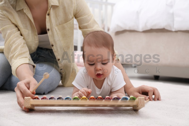 Cute baby and mother playing with xylophone on floor at home