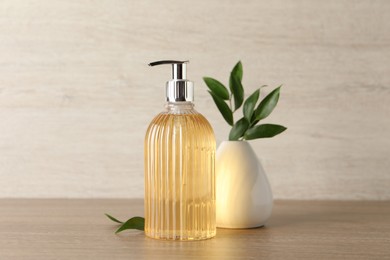 Stylish dispenser with liquid soap and green leaves in vase on wooden table