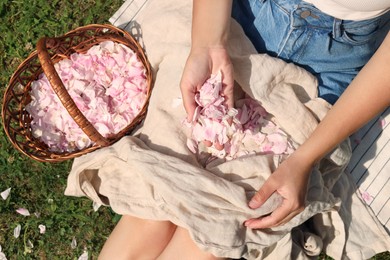 Photo of Woman with basket of beautiful tea rose petals on green grass, top view