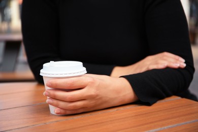 Photo of Woman with cardboard cup of coffee at table, closeup