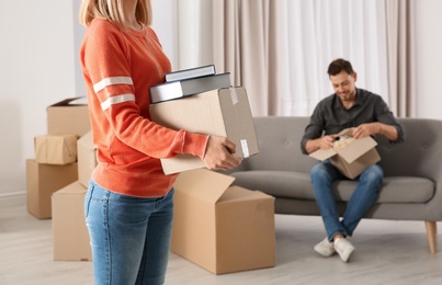 Woman carrying box full of books while man unpacking other in new house. Moving day