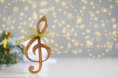 Wooden music note with golden bow on light grey table against blurred Christmas lights. Space for text